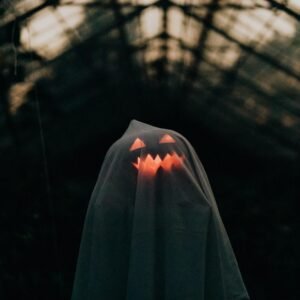 A ghostly figure with a glowing pumpkin face under a sheet in an eerie, dark setting. Perfect Halloween imagery.
