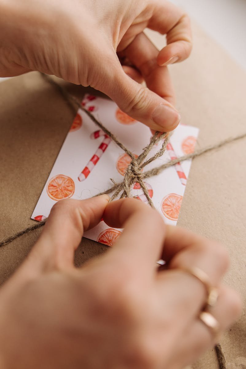 Close-up of hands tying twine on a gift with festive card, symbolizing care and creativity.